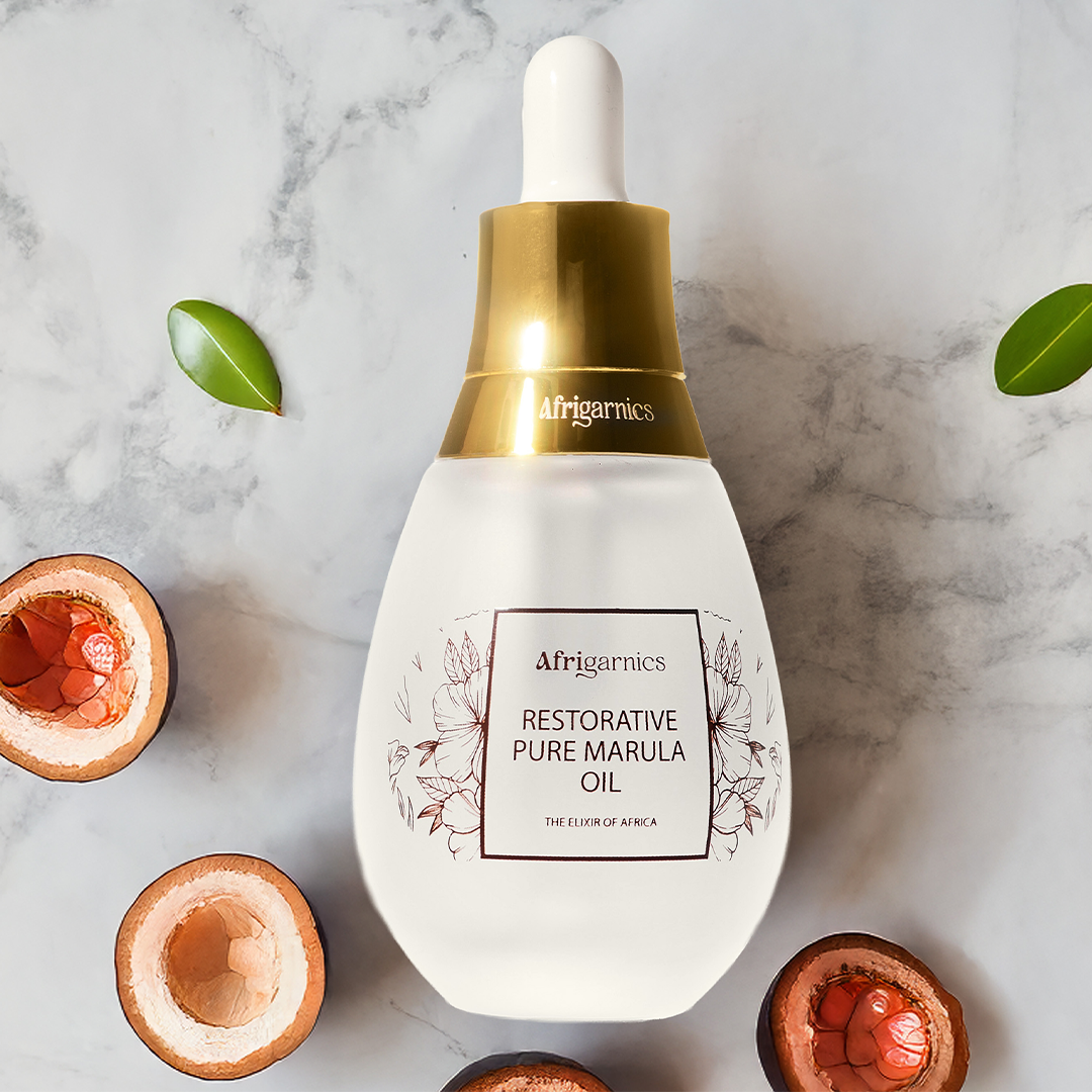 Afrigarnics Restorative Pure Marula Oil bottle on a marble background with marula fruit and leaves.