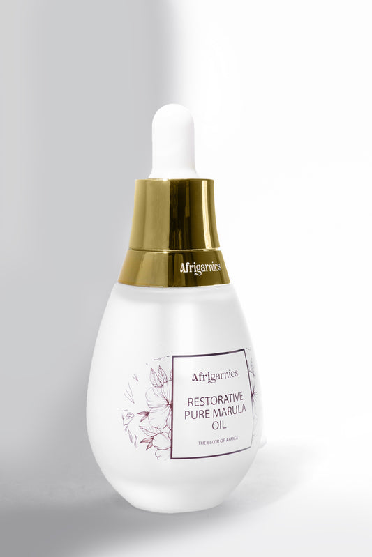 Afrigarnics Restorative Pure Marula Oil bottle on a marble background with marula fruit and leaves.